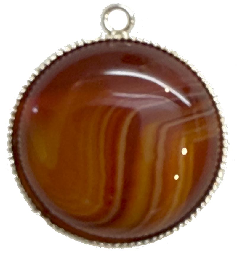 Vor weissem Hintergrund ein rundes Amulett mit silberner Fassung und braun-gemastertem Stein