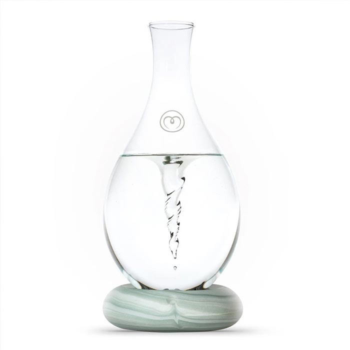Eine tropfenförmige Glaskaraffe mit Wasser gefüllt vor weissem Hintergrund. Das Wasser zeigt einen tiefen Strudel