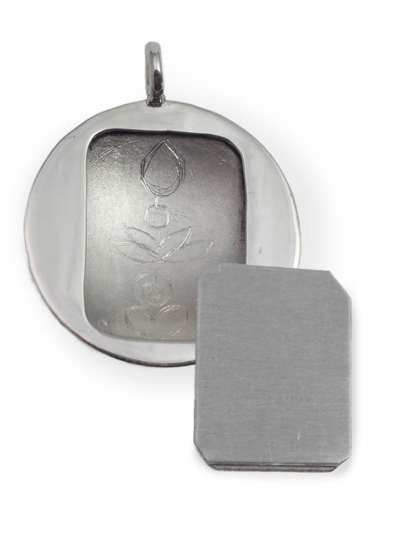 Vor weissem Hintergrund ein rundes, silbernes Amulett, in der Mitte geöffnet, mit einer Blume eingraviert