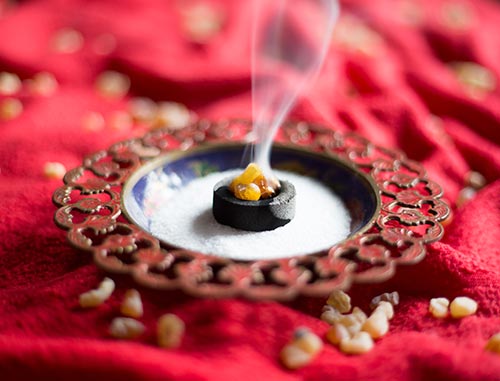 Myrrhe kann auf Kohle geräuchert werden Auf einem knallroten, gerafften Tischtuch steht eine metallene Räucherschale mit Sand, Kohle und Myrrhe darauf