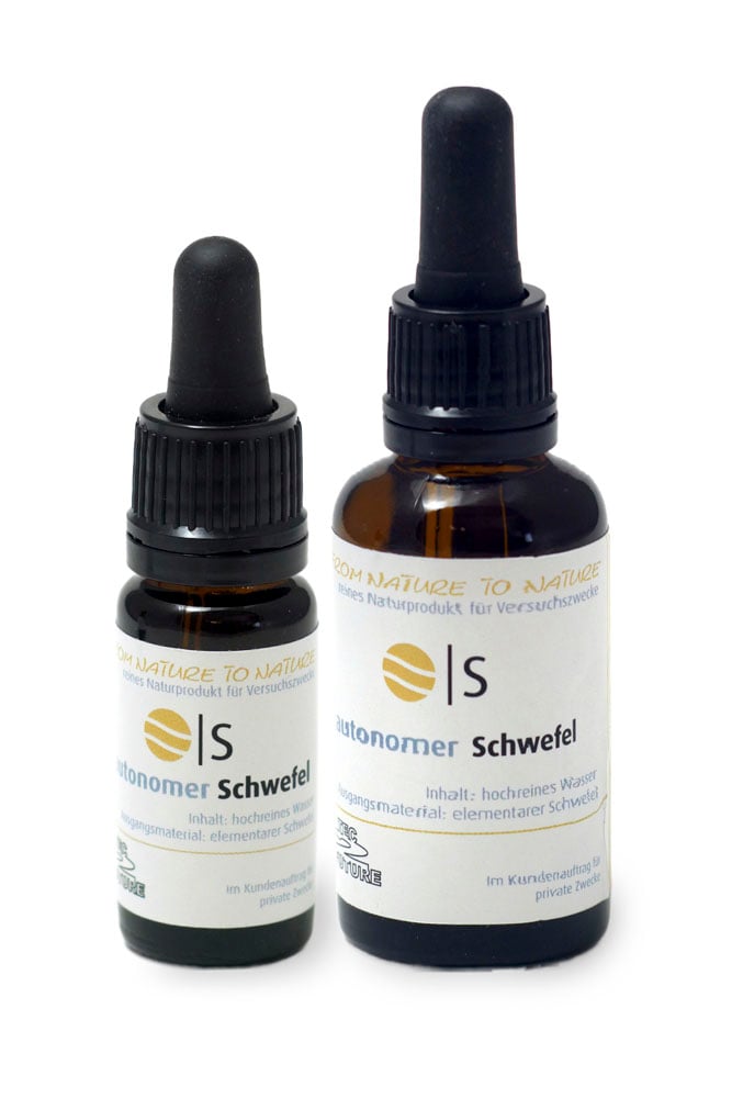 Vor weissem Hingergrund zwei verschieden grosse, braune Glasflaschen mit schwarzem Pipettenverschluss, links die kleinere, auf jeder Flasche ein weisses Etikett mit der Aufschrift "autonomer Schwefel"