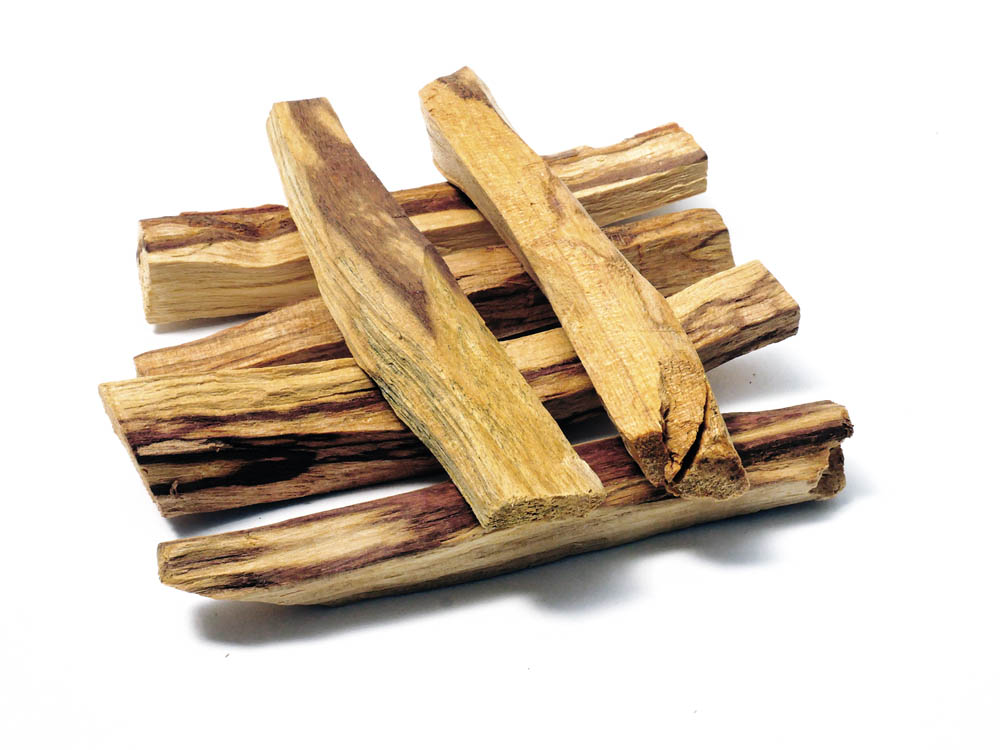 Vor weissem Hintergrund sechs unregelmässige Holzstäbchen Palo Santo kreuz und quer, das Holz ist hell und dunkel gestreift