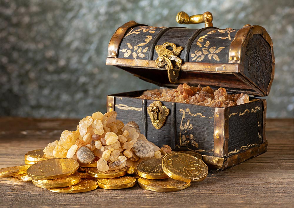 Auf einem Holztisch liegen Goldmünzen, Weihrauch-Harz und eine braun-goldene Schatztruhe gefüllt mit Myrrhe