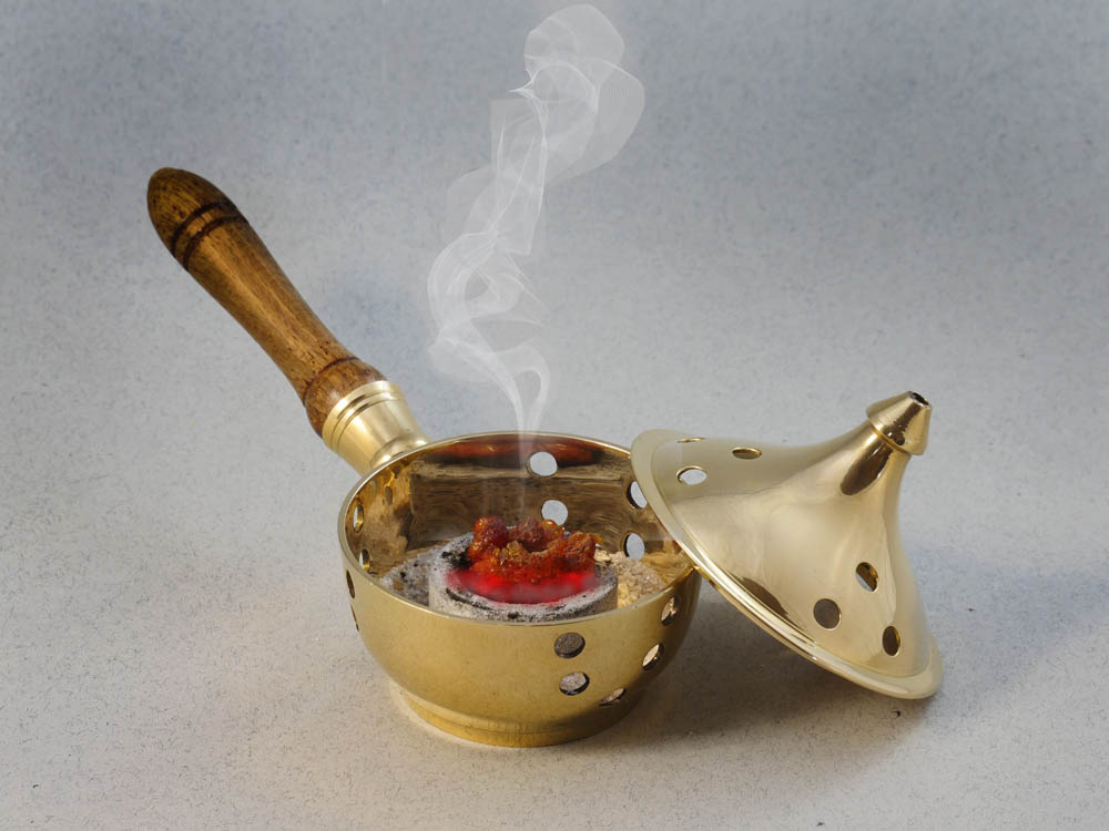Vor grauem Hintergrund ein goldfarbenes Räuchergefäss, in dem Myrrhe auf glimmender Kohle raucht