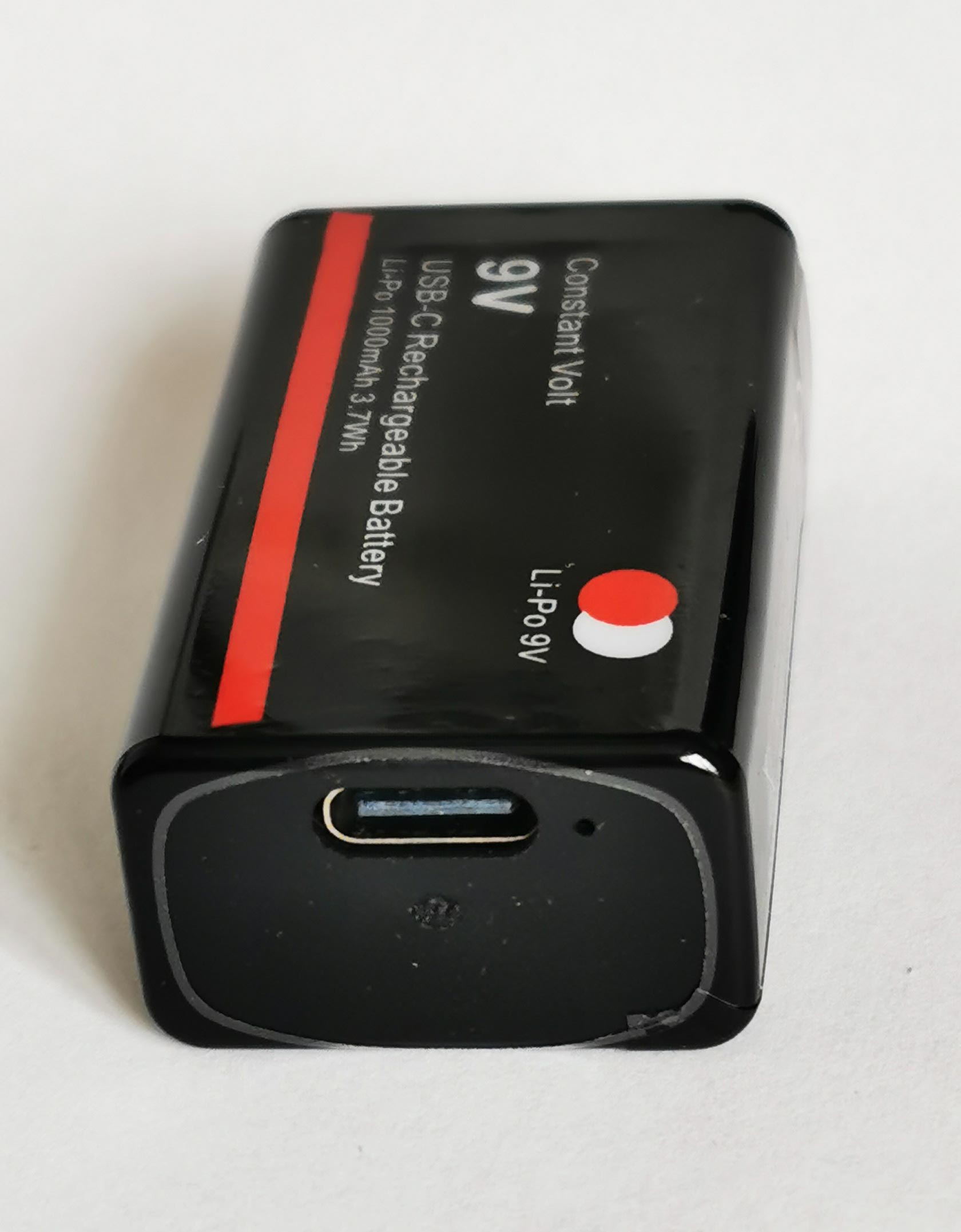 Schwarzer, rechteckiger 9 Volt Akku liegend mit USB-Eingang, längs ein roter Streifen, vor weissem Hintergrund
