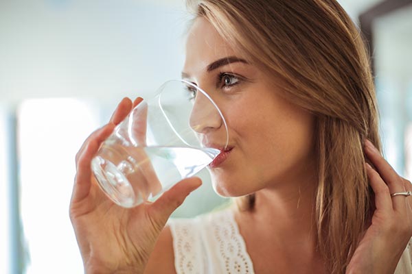 Hübsche, blonde, junge Frau trinkt aus einem Glas Wasser