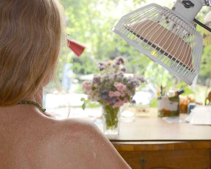 Vorschau: TDP-Lampe Doppelkopf Vorschau: Eine weisse Stehlampe vor lila Hintergrund mit zwei Armen und zwei Therapieköpfen zur Abstrahlung der Infrarot Wärmelampe