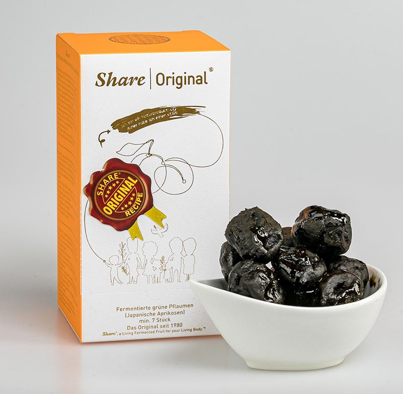 Vorschau: Die Share Pflaume kaufen Vorschau: Eine kleine neben einer grossen Verpackung, beide sind weiss-orange. Davor ein weisses Schälchen mit schwarzen, glänzenden, schrumpeligen Pflaumen