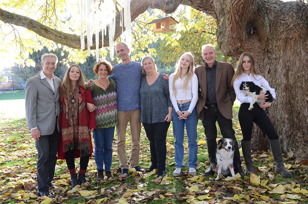 Acht Menschen mit zwei Hunden vor einem grossen Baum mit bunten Herbstblättern