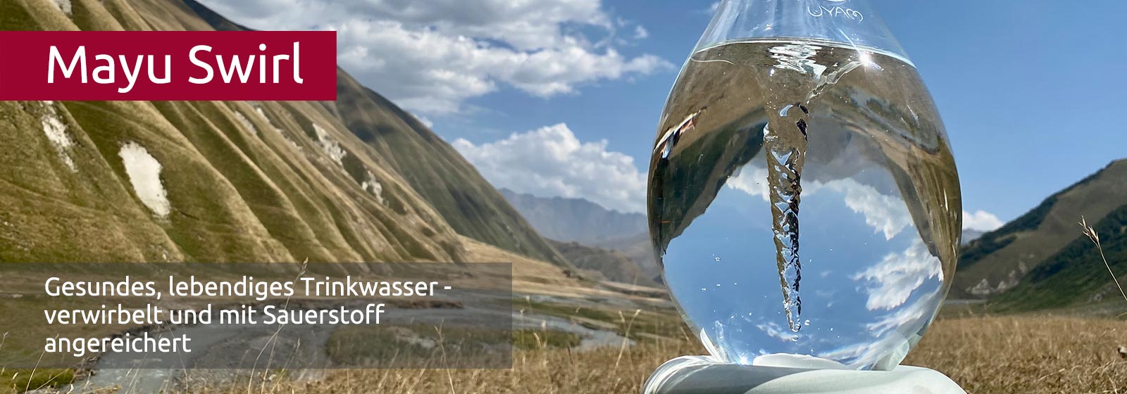 Eine durchsichtige Glaskaraffe mit Wasser und einem Strudel, in dem sich umliegenden Berge verkehrt herum brechen