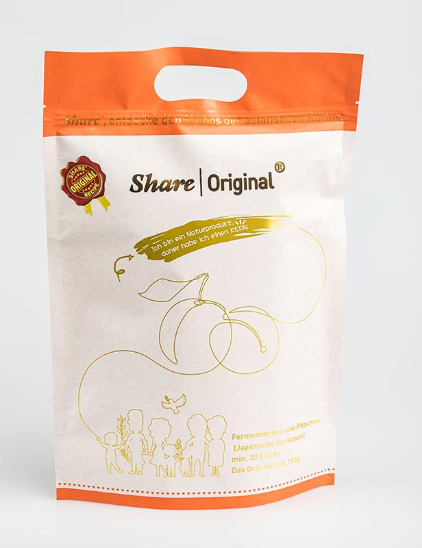 Vorschau: Die Share Pflaume kaufen Vorschau: Eine kleine neben einer grossen Verpackung, beide sind weiss-orange. Davor ein weisses Schälchen mit schwarzen, glänzenden, schrumpeligen Pflaumen