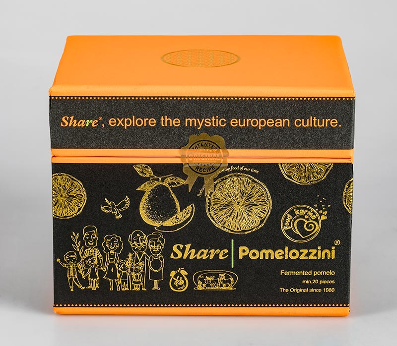 Vorschau: Die Share Pomelozzini Vorschau: Ein braun-orange-farbiger Karton steht hochkant vor weissem Hintergrund. Darauf in gold die Worte Share Pomelozzini und Bilder von Pampelmusen