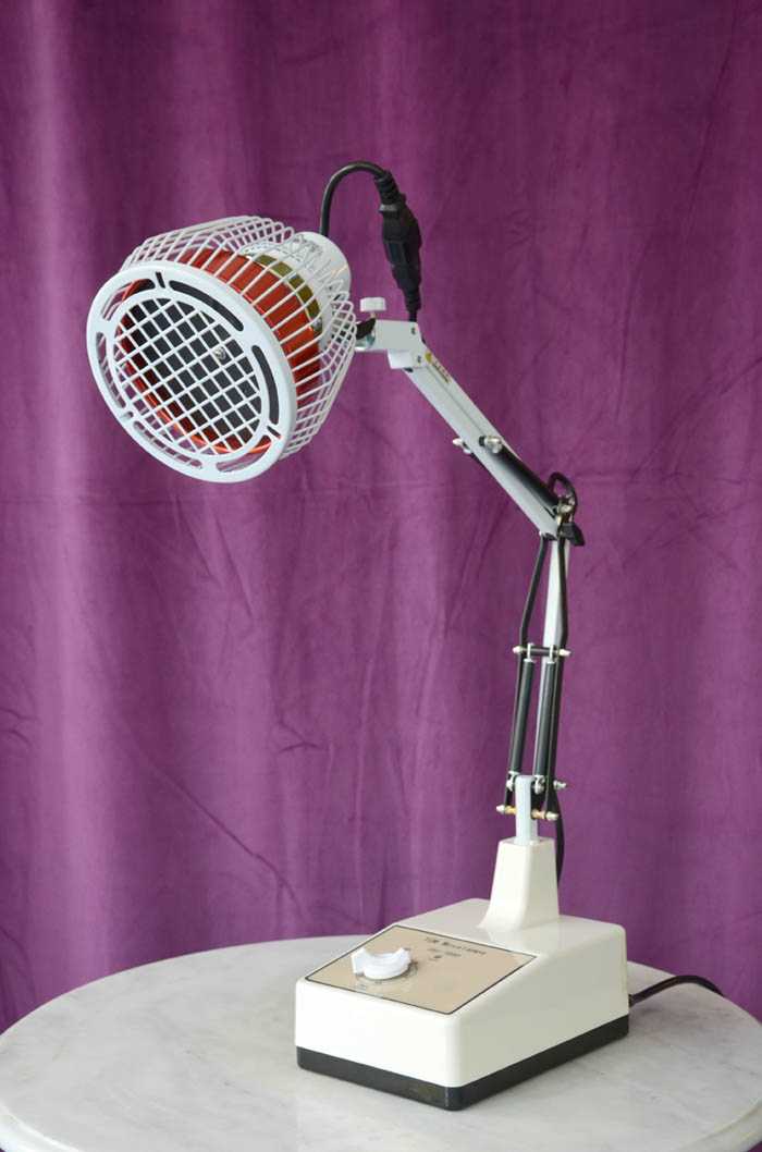 Eine weisse Tischlampe vor lila Hintergrund mit Therapiekopf zur Abstrahlung der heilenden Wärme 