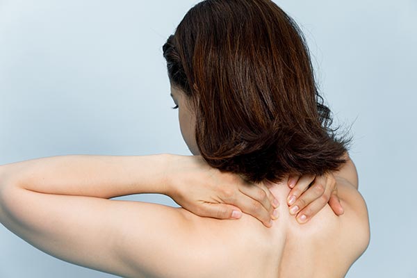 Brünette Frau massiert ihre Nackenmuskeln, um das Magnesiumöl zu verteilen