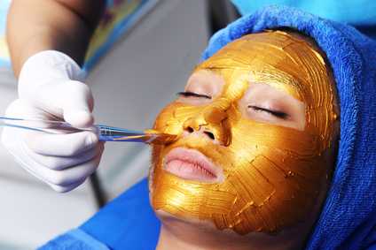 Auftragen von Gold auf das Gesicht einer Frau. Verjüngender Effekt von Goldkolloid