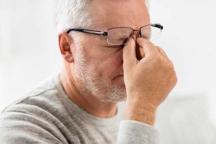 Ein älterer Mann mit weißem Vollbart ist müde und kneift sich mit geschlossenen Augen die Stirn