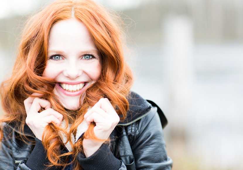 Lachende Frau fasst sich in ihre schönen, roten, langen Haare